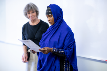 Adult ESL learner reading a paper with volunteer standing close beside her